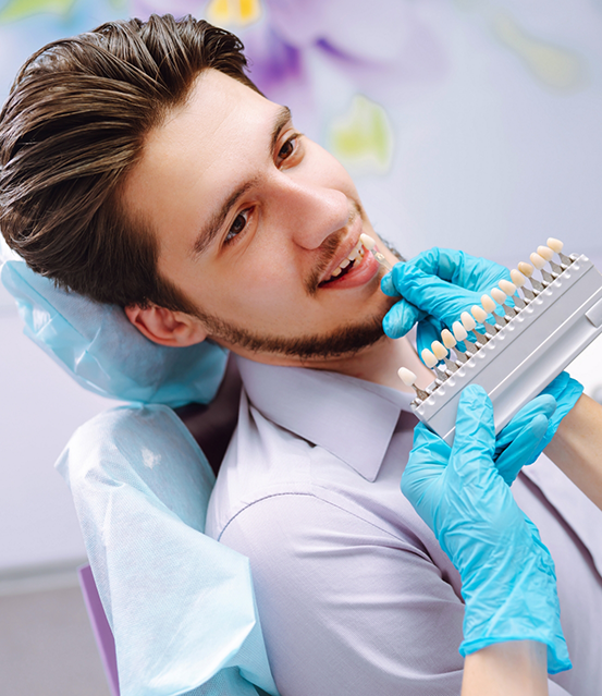 Dentist holding a veneer in front of a patient's teeth