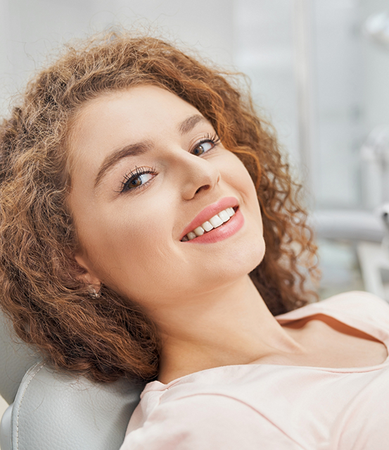 Woman with curly brown hair smiling in the dental chair