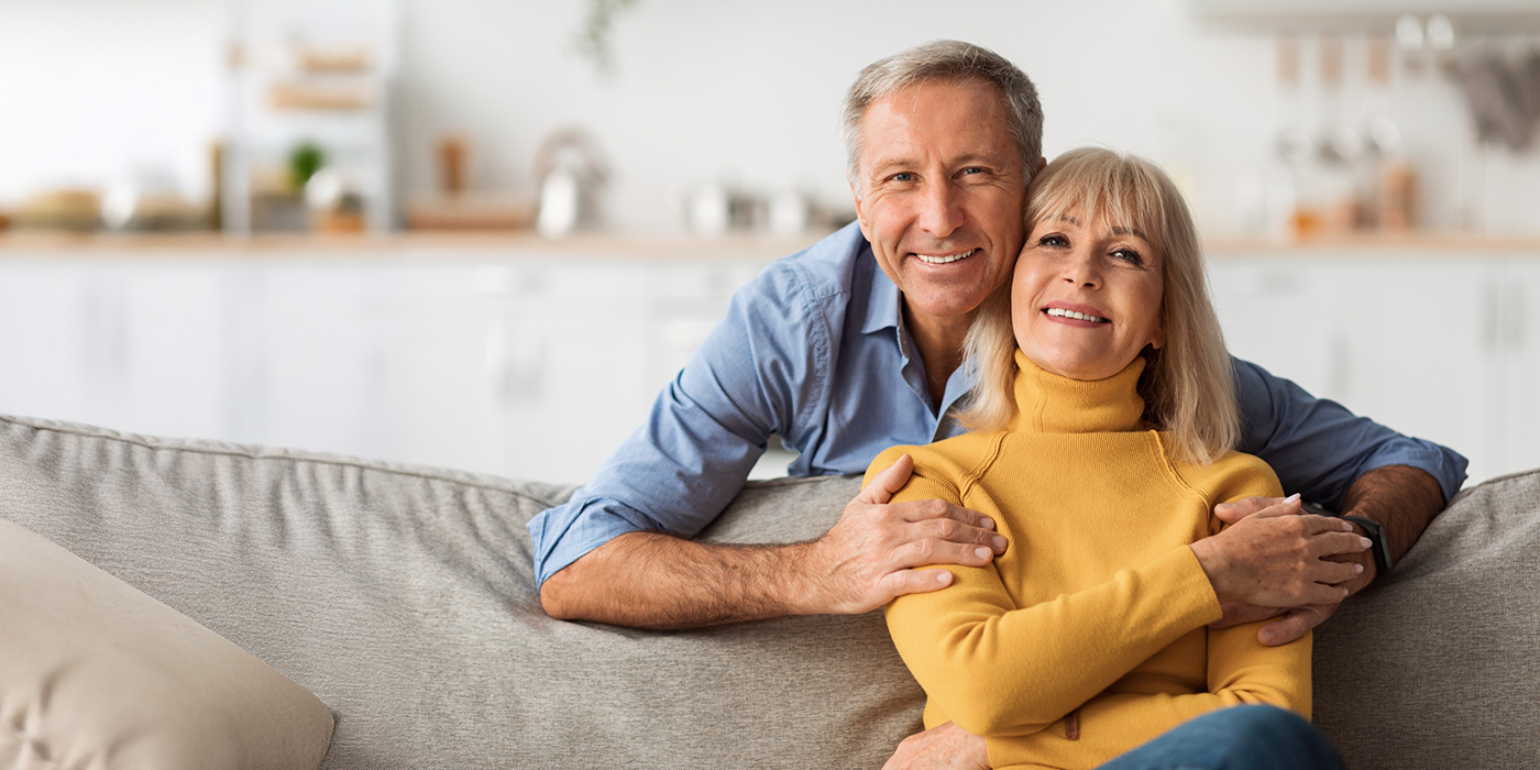 Older couple at home smiling with dental crowns in Fort Worth