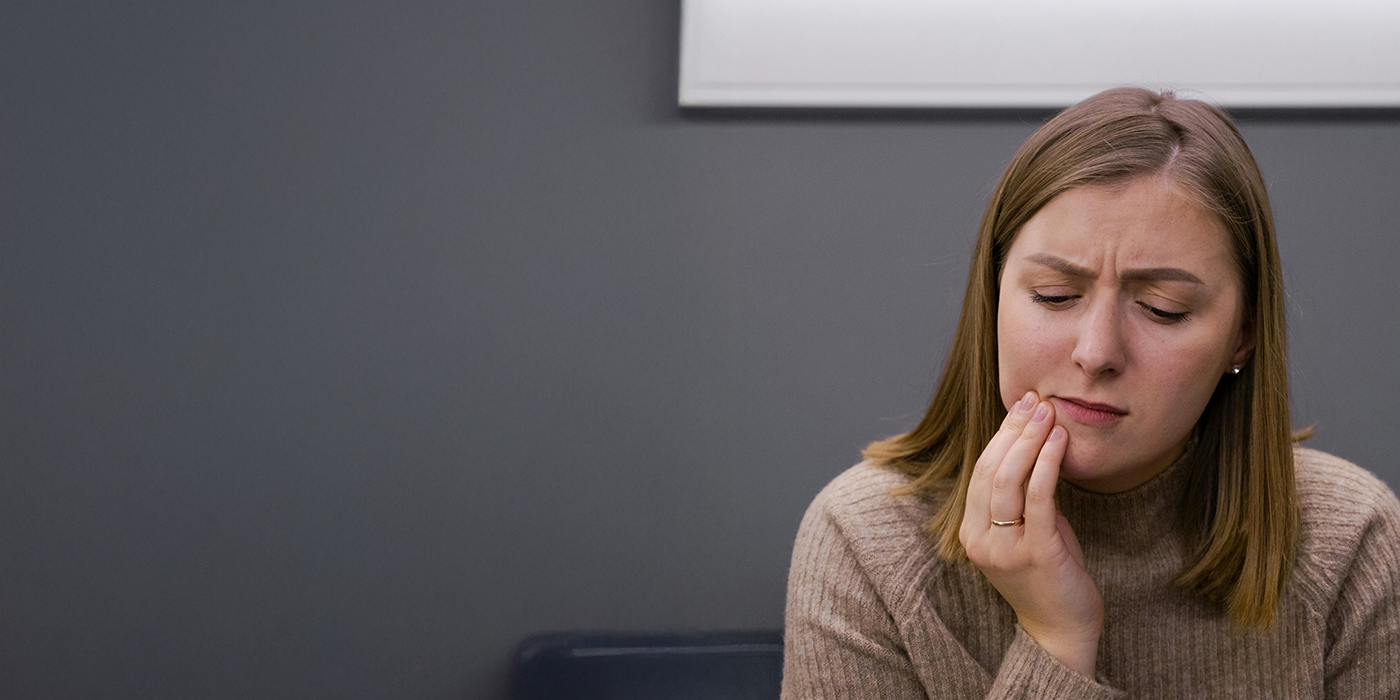 Woman holding her cheek in pain before seeing an emergency dentist in Fort Worth