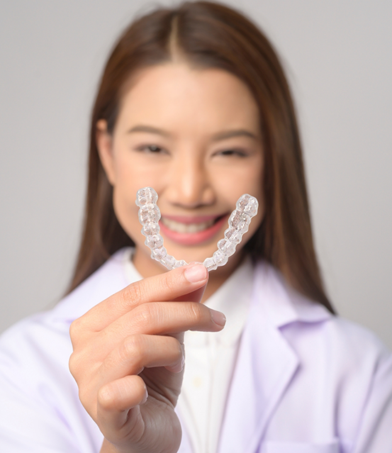 Smiling woman holding an Invisalign clear aligner
