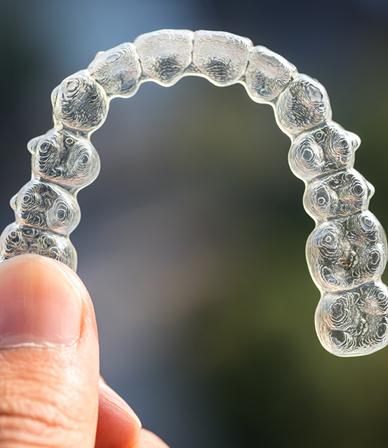 Close up of a hand holding a clear aligner