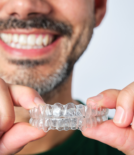 Smiling man holding two Invisalign aligners