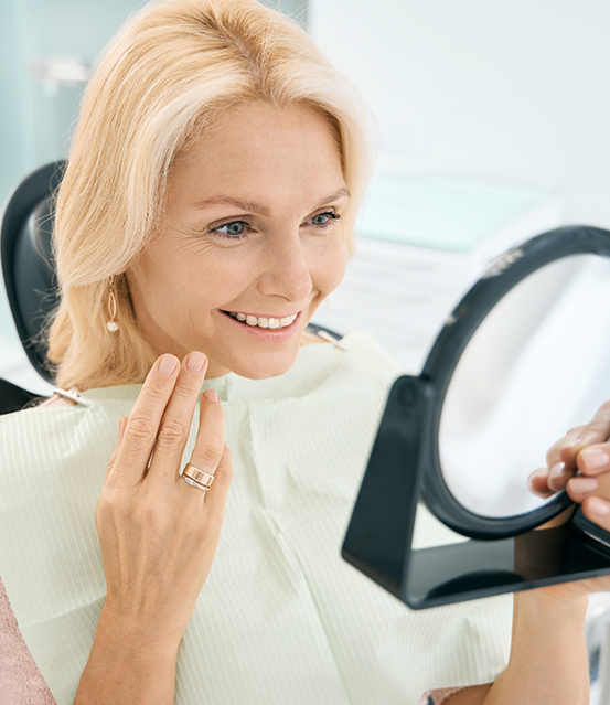 Woman in the dental chair looking at her smile in a mirror